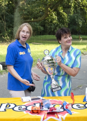 2015 Gayle Tufts und Kerstin Gerke 2015 Gayle Tufts und Kerstin Gerke. Gayle Tufts hält den Wanderpokal von HfH in der Hand. Neben ihr steht Kerstin Gerke, sie trägt das T-Shirt von HfH. Vor den beiden ist ein Tisch mit einer gelben Tischdecke aufgebaut. Die Tischdecke hat das Logo von Pedigree. Auf dem Tisch liegen mehrere kleine Bälle als Preise für Hundebesitzer.