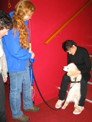 2011 Moby in der Pause mit Gayle Tuffts 2011 Moby in der Pause mit Gayl Tuffts. Gayle Tuffts sitzt auf einer Treppe und kuschelt mit dem hellen Golden Retriever Welpen Mobi. Mobi trägt ein schwarzes Geschirr und eine schwarze Leine. Daneben steht Kerstin Gerke und hält die Leine fest.